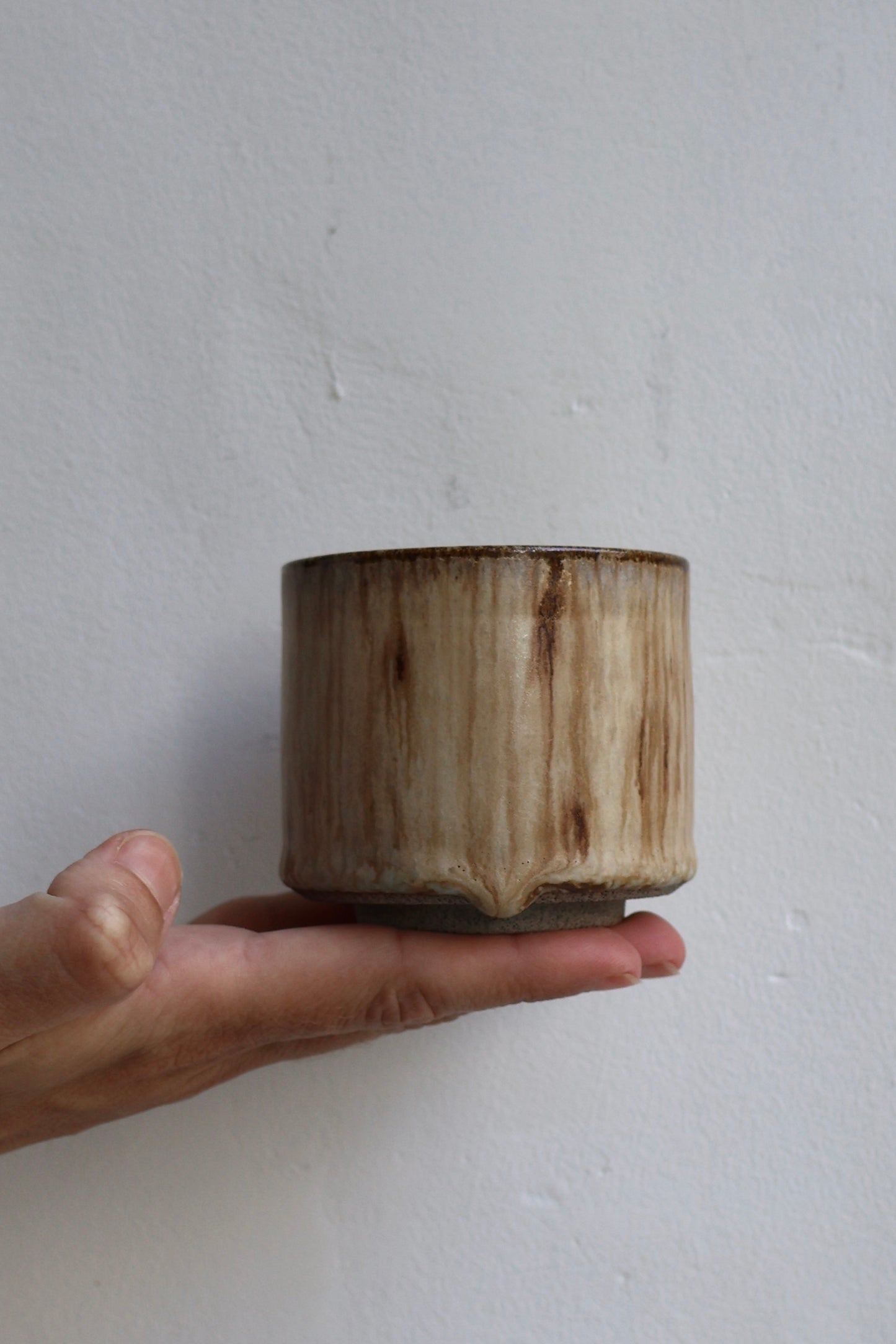 Hand holding a small cylindrical ceramic vase against a plain background