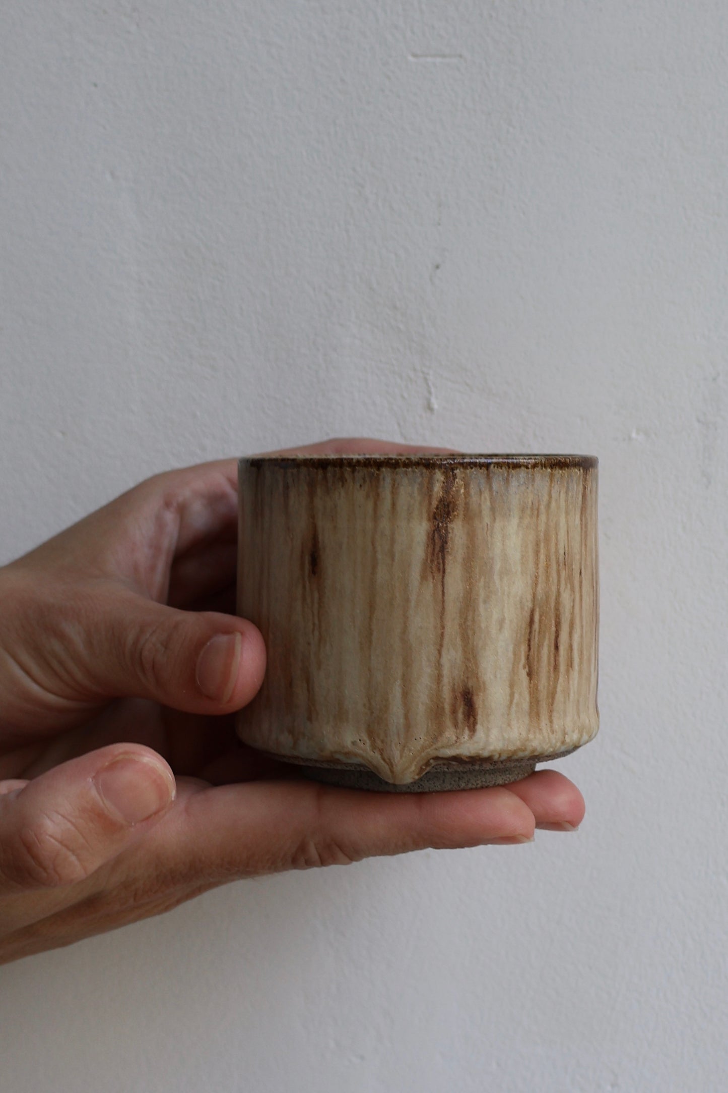 Hand holding a small ceramic cup against a plain background